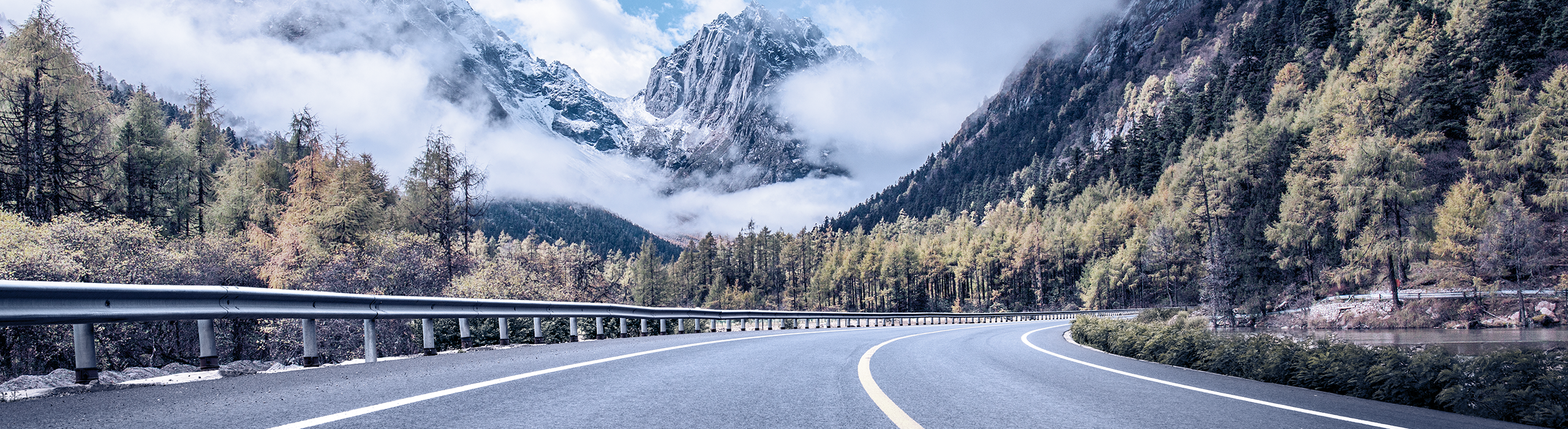 View of Western Canada highway amidst evergreen forest and snowy mountains